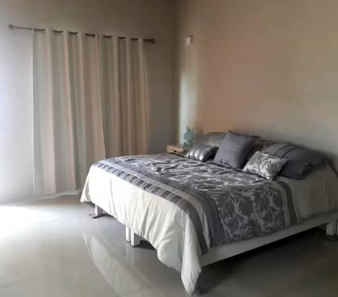 Cama vestida en colcha color gris con almohadas y cojines en color gris